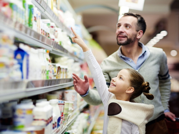 Un père et sa fille parcourent les allees d'une supermarche, la petite fille montre du doigt des produits sur une etagere